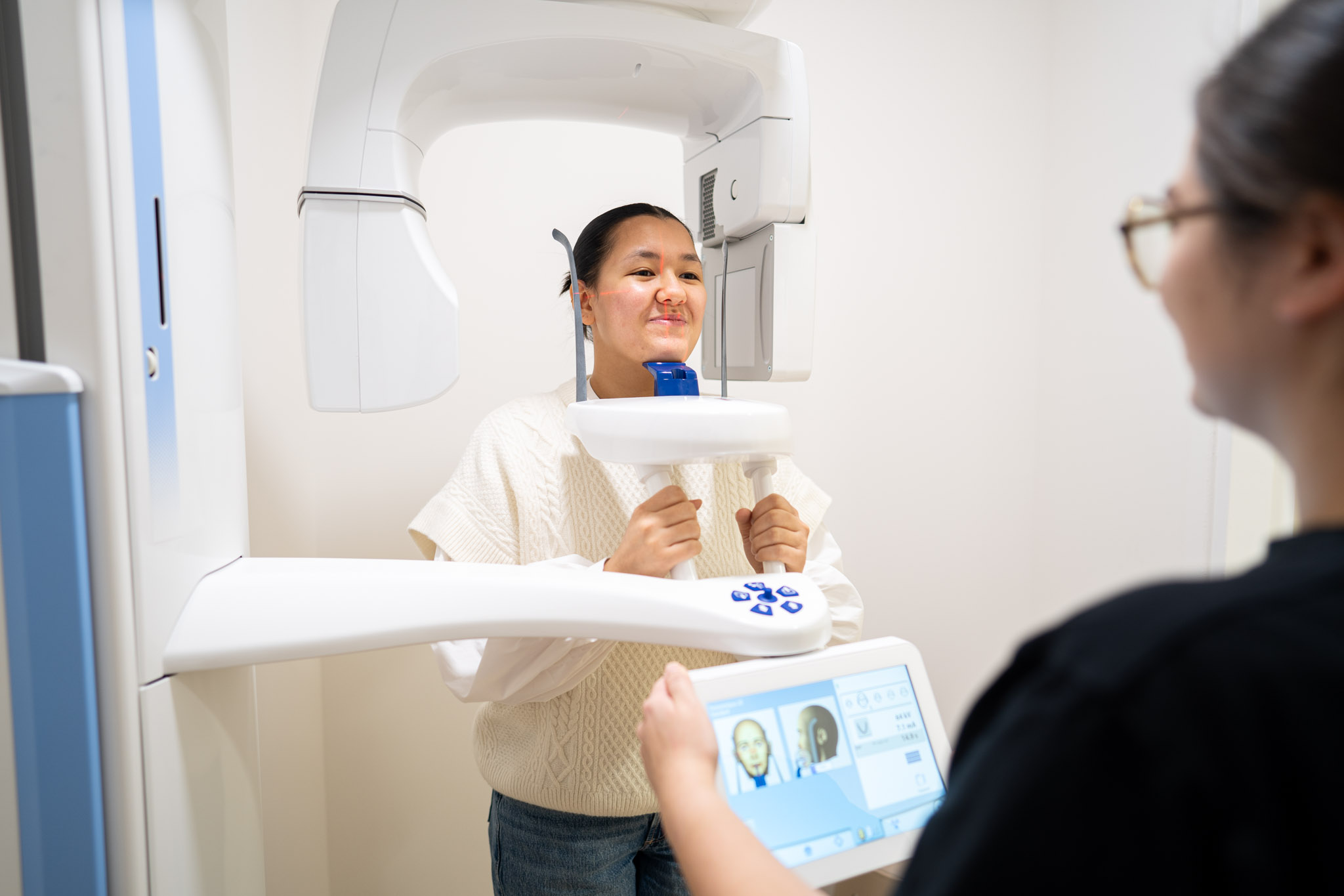 Une patiente installée debout dans l'appareil de radiographie panoramique, accompagnée par une assistante